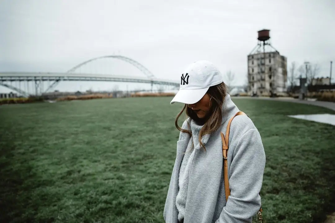 Person in weißer NY Baseballkappe und grauem Pullover mit neuester Streetwear.